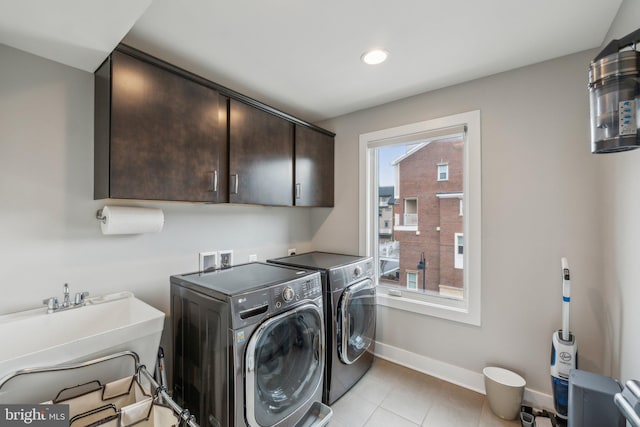 clothes washing area featuring light tile patterned floors, baseboards, washing machine and clothes dryer, cabinet space, and a sink