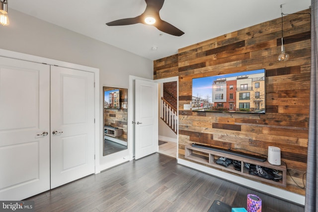 interior space with stairway, wood walls, a ceiling fan, and wood finished floors