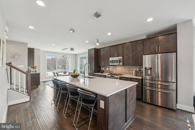 kitchen with a kitchen island with sink, a sink, stainless steel appliances, dark brown cabinets, and a kitchen breakfast bar