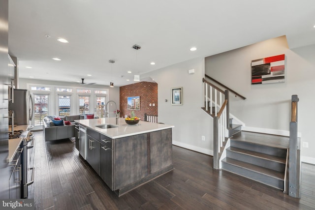 kitchen featuring a sink, open floor plan, a center island with sink, appliances with stainless steel finishes, and dark wood-style flooring