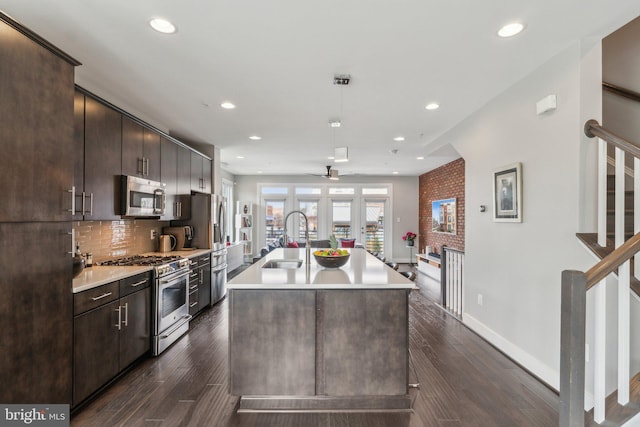 kitchen with dark brown cabinets, light countertops, decorative backsplash, appliances with stainless steel finishes, and a sink