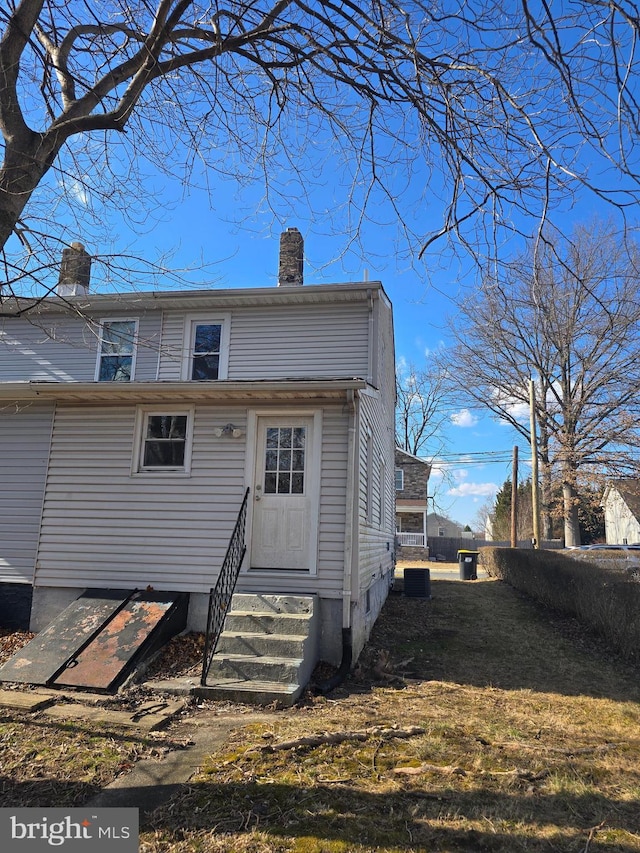 back of house with entry steps, central AC, and a chimney