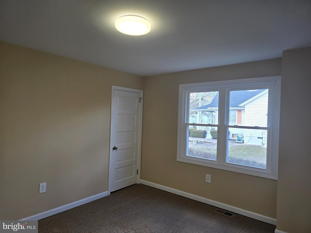 empty room featuring visible vents, dark carpet, and baseboards