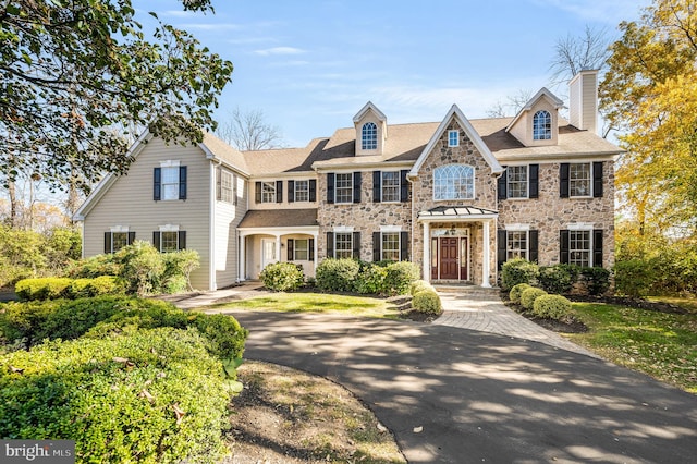 colonial-style house featuring stone siding and a chimney