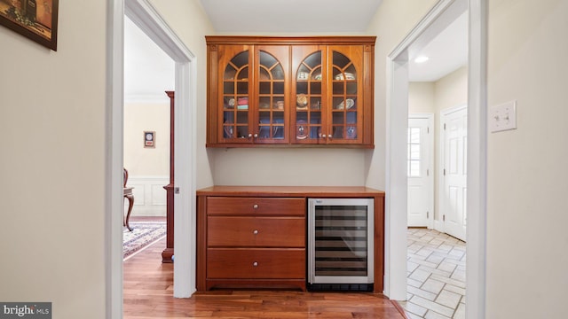 bar with a dry bar, beverage cooler, light wood-style floors, and wainscoting