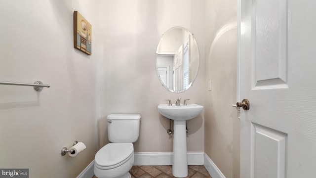 half bath featuring a sink, stone finish flooring, baseboards, and toilet