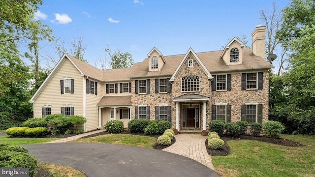 colonial home featuring a front lawn, stone siding, and a chimney