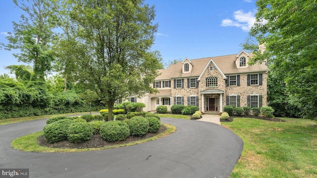 view of front of property with a front lawn, stone siding, and curved driveway