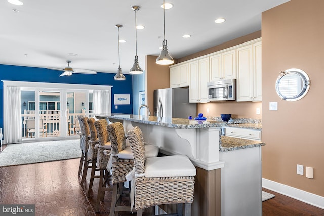 kitchen featuring a breakfast bar, dark wood-style floors, baseboards, and appliances with stainless steel finishes