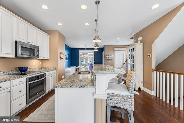 kitchen with a breakfast bar, a sink, white cabinetry, stainless steel appliances, and dark wood-style flooring