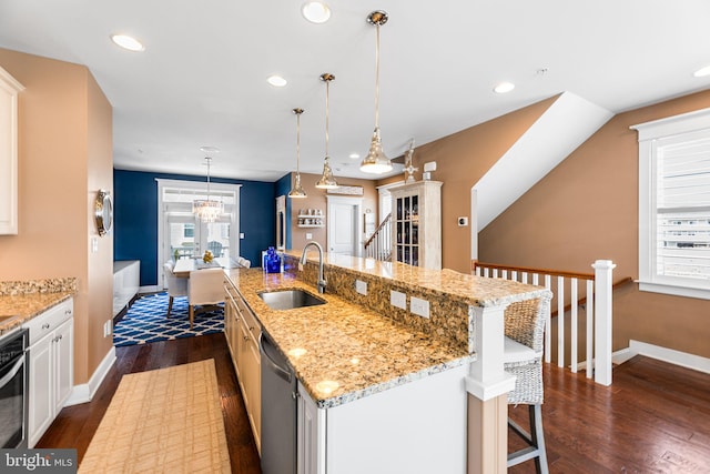 kitchen with a kitchen island with sink, a sink, dark wood finished floors, a breakfast bar area, and dishwasher