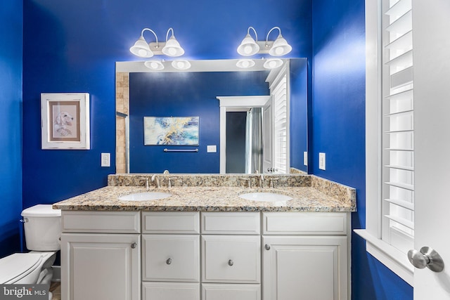 bathroom with a sink, toilet, and double vanity