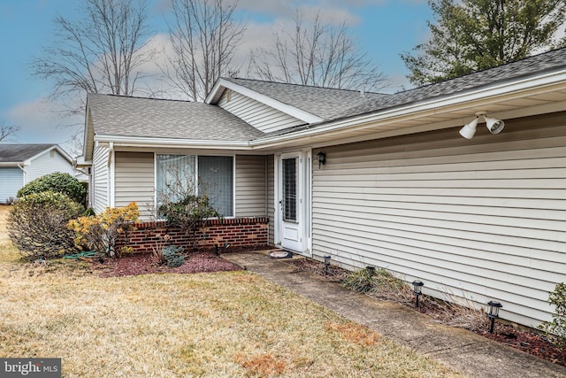 property entrance featuring a lawn and roof with shingles