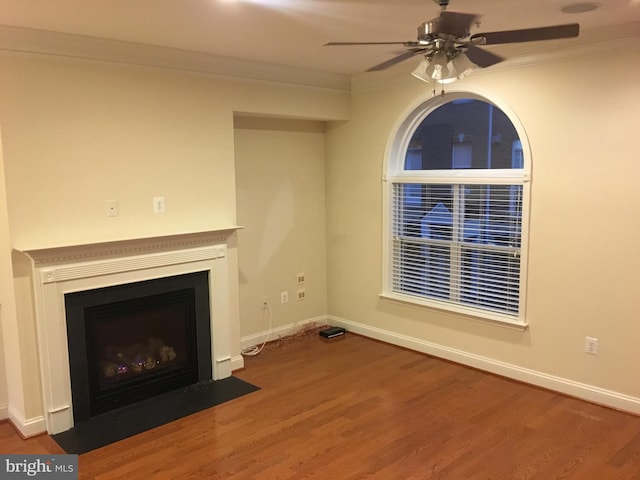 unfurnished living room with a fireplace with flush hearth, a ceiling fan, wood finished floors, crown molding, and baseboards