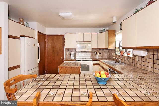 kitchen with white appliances, tile countertops, a peninsula, a sink, and tasteful backsplash