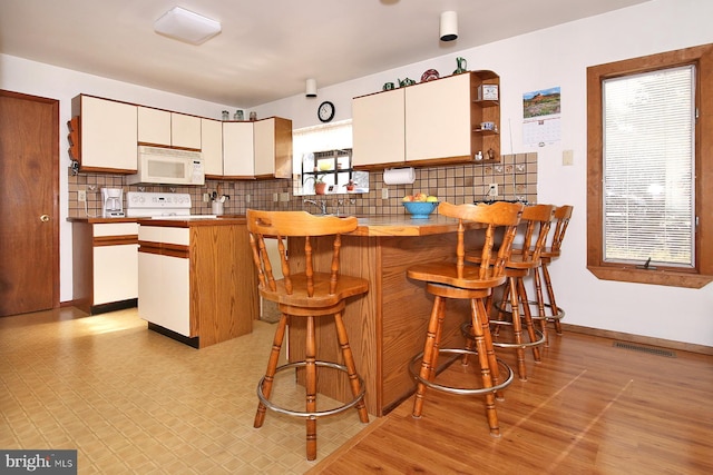 kitchen featuring white microwave, visible vents, decorative backsplash, a peninsula, and white cabinets