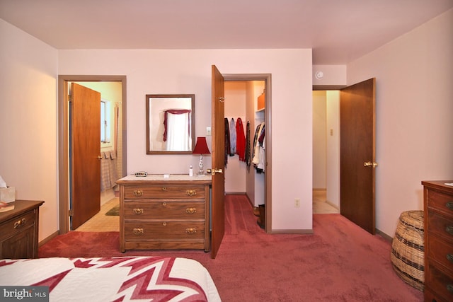 bedroom featuring a walk in closet, ensuite bath, baseboards, and dark carpet