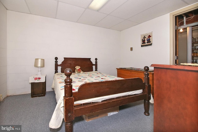 carpeted bedroom with concrete block wall and a paneled ceiling