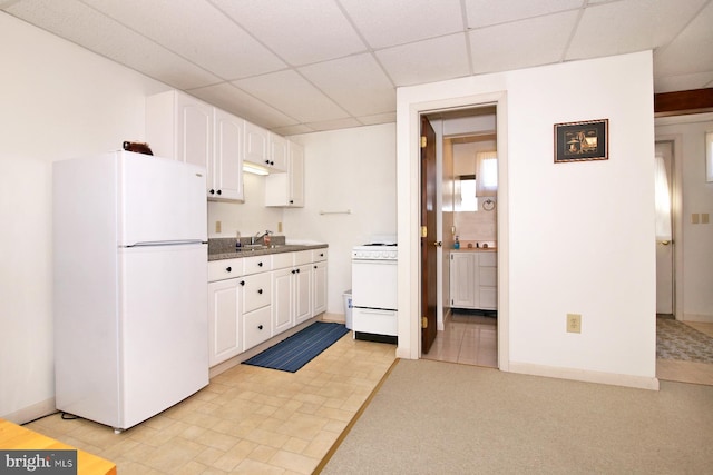 kitchen with dark countertops, white cabinets, white appliances, a paneled ceiling, and a sink