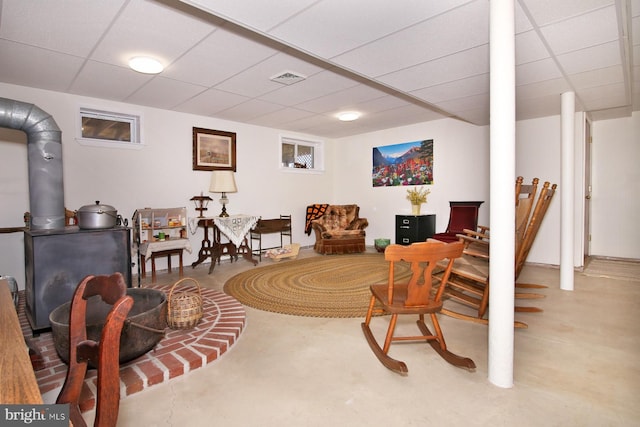 sitting room featuring a drop ceiling, concrete flooring, a wood stove, and visible vents