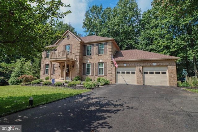 colonial-style house with a front yard, brick siding, a balcony, aphalt driveway, and an attached garage