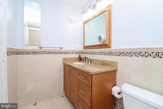 bathroom featuring toilet, tile walls, visible vents, and a wainscoted wall