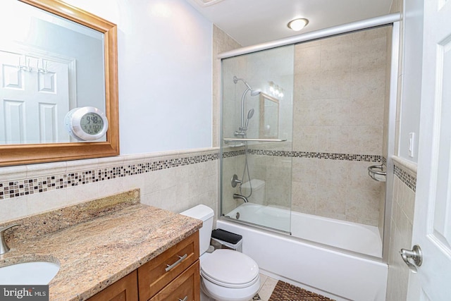 full bathroom with vanity, wainscoting, shower / bath combination with glass door, toilet, and tile walls