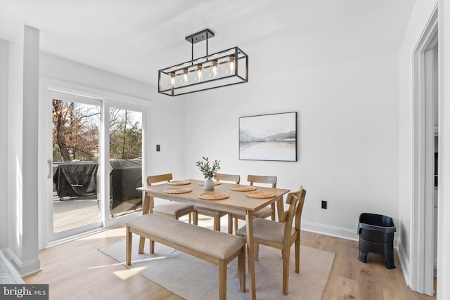 dining space with a notable chandelier, baseboards, and light wood-type flooring