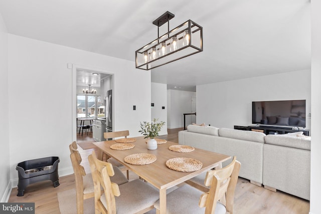 dining room with a chandelier, light wood finished floors, and baseboards