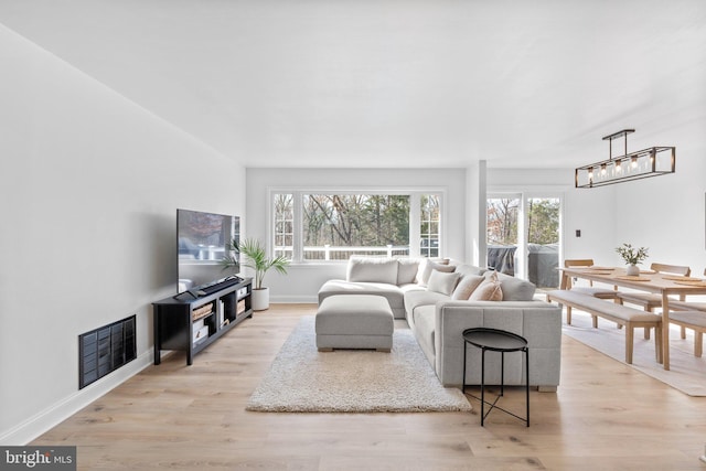 living area with a chandelier, visible vents, light wood-type flooring, and baseboards