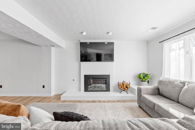 living area with visible vents, a brick fireplace, crown molding, baseboards, and wood finished floors