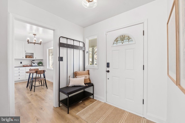 entryway with light wood finished floors, a chandelier, and baseboards