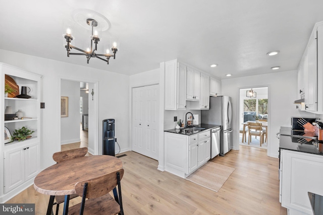 kitchen with a sink, light wood-style floors, dishwasher, dark countertops, and a notable chandelier