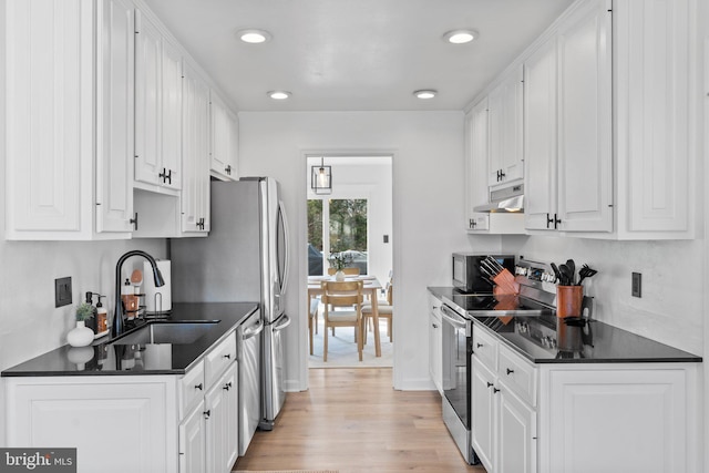 kitchen with under cabinet range hood, a sink, dark countertops, stainless steel appliances, and white cabinets