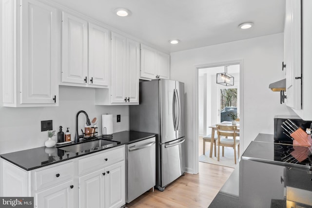 kitchen featuring a sink, light wood-style floors, appliances with stainless steel finishes, white cabinetry, and wall chimney range hood