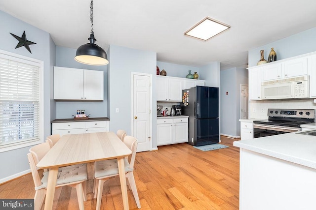 kitchen with white microwave, stainless steel range with electric stovetop, white cabinetry, and freestanding refrigerator