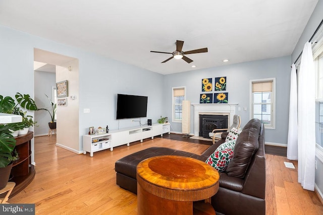 living room with baseboards, a fireplace with flush hearth, recessed lighting, light wood-style floors, and a ceiling fan