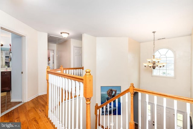 hall featuring an upstairs landing, light wood-style flooring, an inviting chandelier, baseboards, and attic access