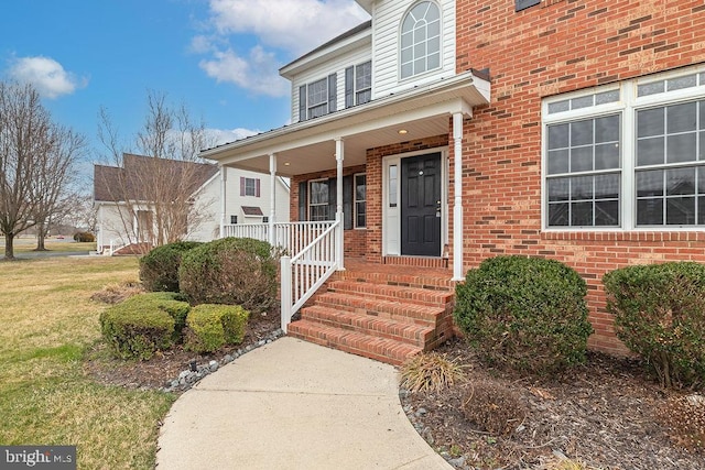 entrance to property with a porch, a lawn, and brick siding