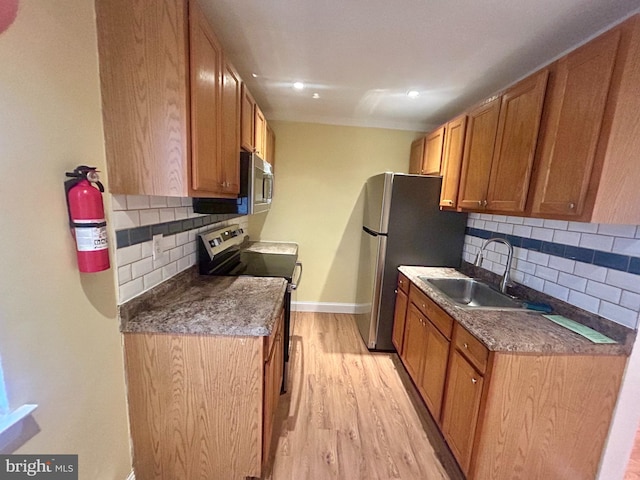 kitchen with a sink, brown cabinets, light wood-style floors, and appliances with stainless steel finishes