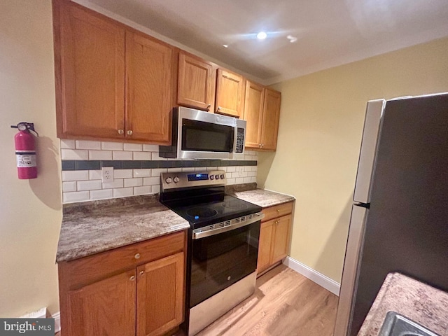 kitchen featuring light wood finished floors, backsplash, baseboards, and appliances with stainless steel finishes