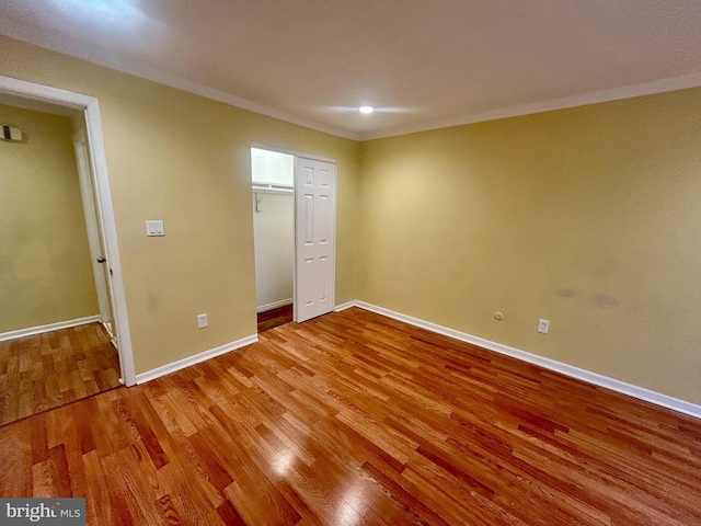 unfurnished bedroom featuring a closet, crown molding, baseboards, and wood finished floors