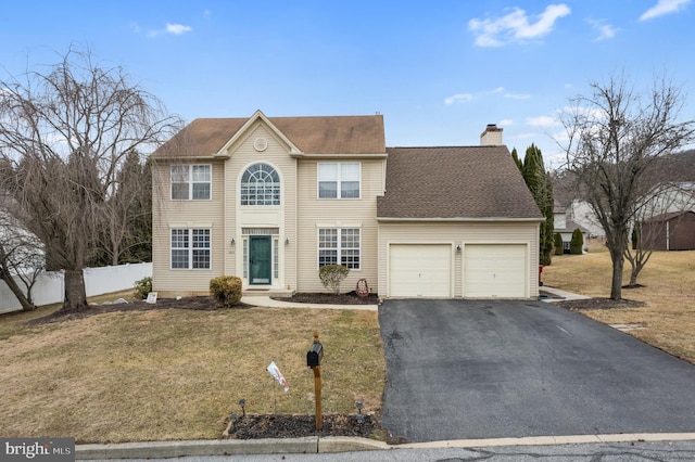 colonial-style house featuring a front yard, fence, an attached garage, a chimney, and aphalt driveway