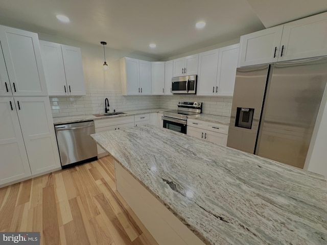 kitchen with light wood-type flooring, a sink, appliances with stainless steel finishes, white cabinets, and decorative backsplash