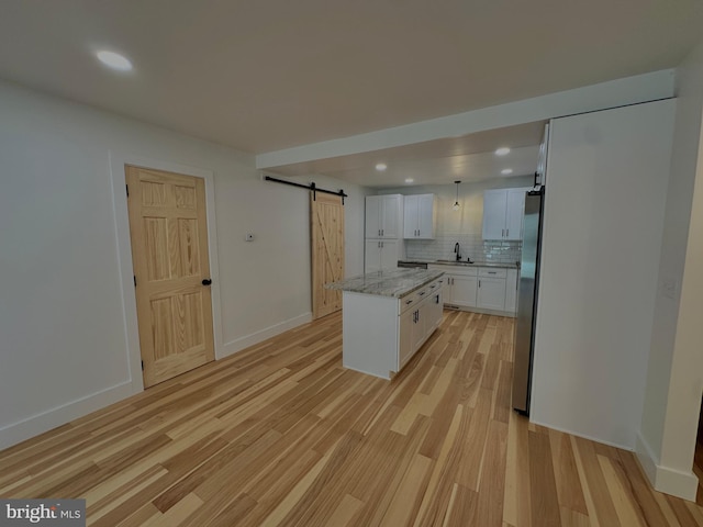 kitchen featuring a barn door, light wood-style flooring, freestanding refrigerator, white cabinets, and a sink