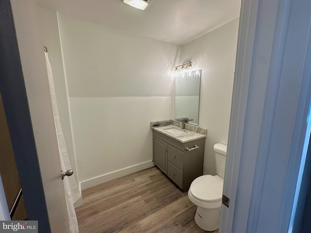 bathroom with baseboards, toilet, vaulted ceiling, wood finished floors, and vanity