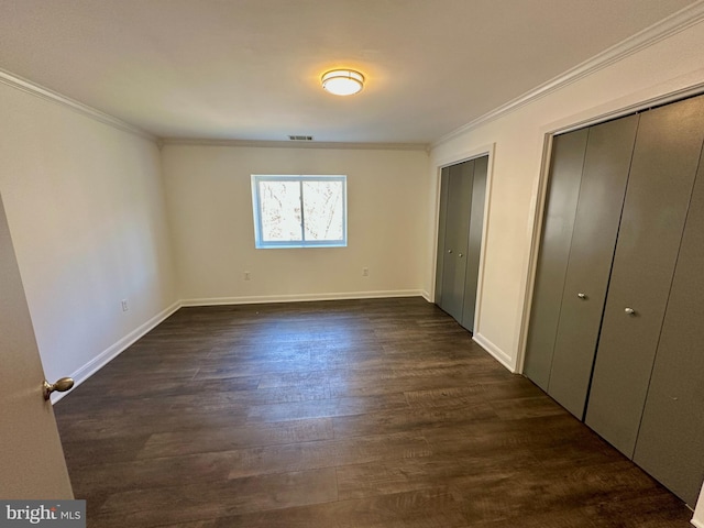 unfurnished bedroom featuring visible vents, two closets, ornamental molding, and dark wood finished floors