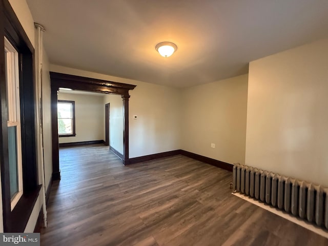 unfurnished room featuring baseboards, dark wood-style floors, and radiator heating unit