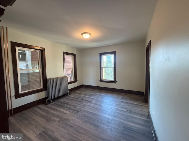 empty room featuring dark wood finished floors, radiator, and baseboards