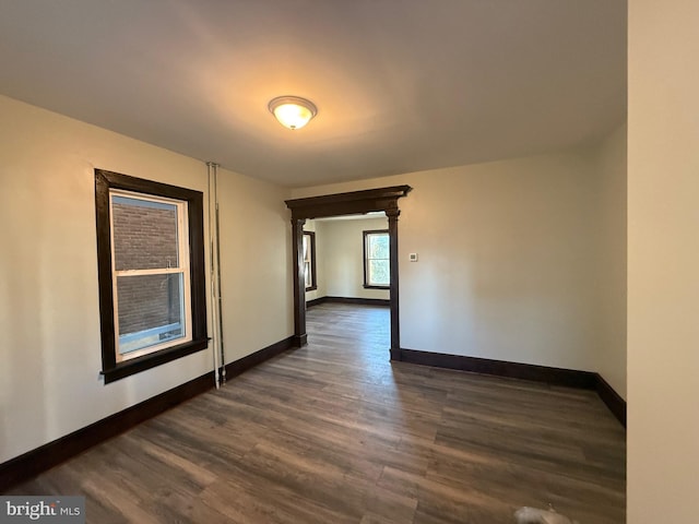 unfurnished room featuring decorative columns, baseboards, and dark wood-style floors